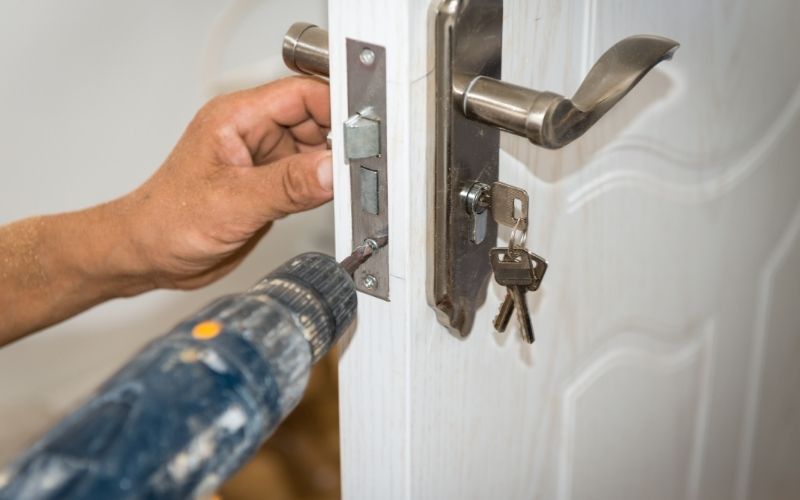 Serrurier fixant une serrure sur une porte avec une visseuse